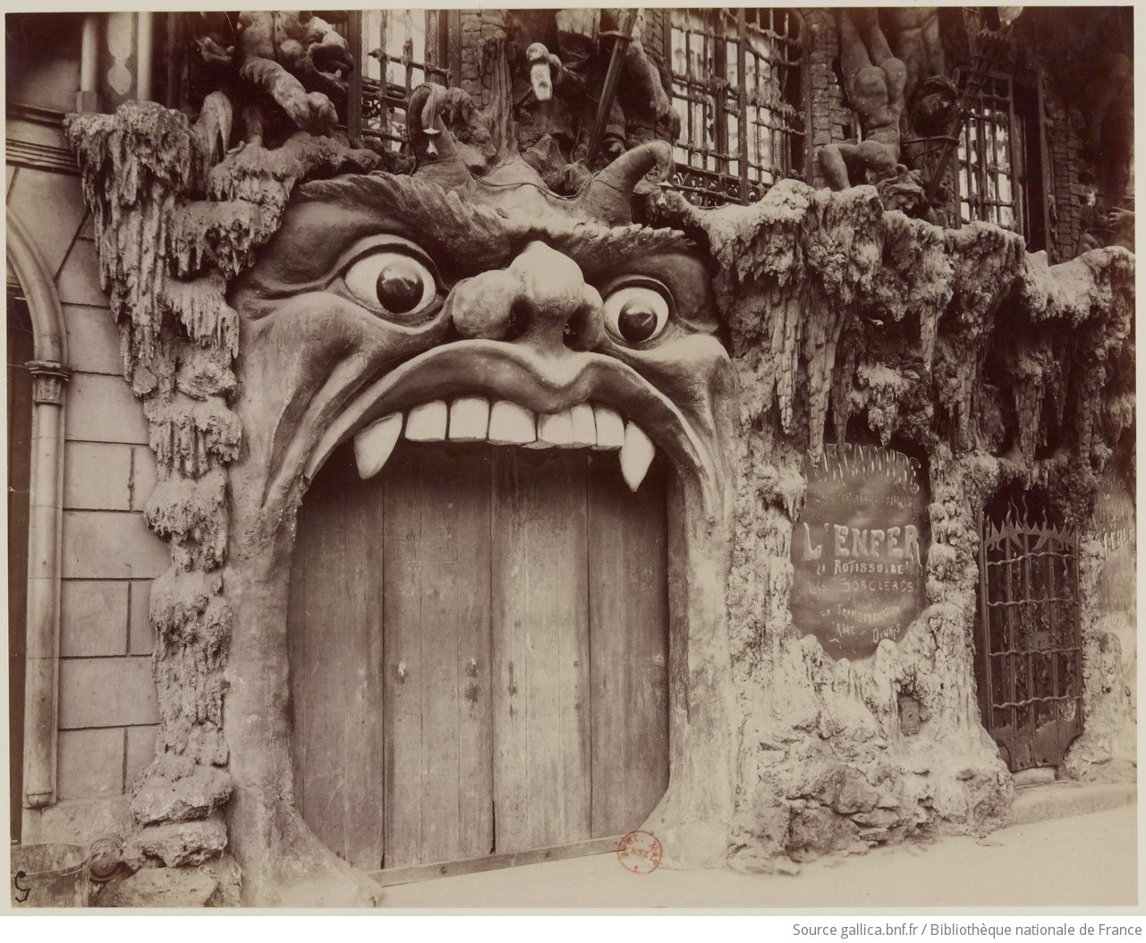 Eugène Atget, "Cabaret de L'Enfer : Bd de Clichy", ca. 1910-12 An early 20th-century, black and white photo of the exterior of the Cabaret de l'Enfer. The door is the mouth of a giant demon, and the rest of the wall is covered with stalagmites and the tormented bodies of sinners